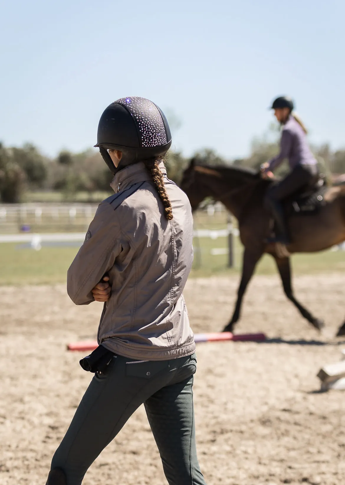 A trainer working a horse from the ground in a sand arena with ground poles