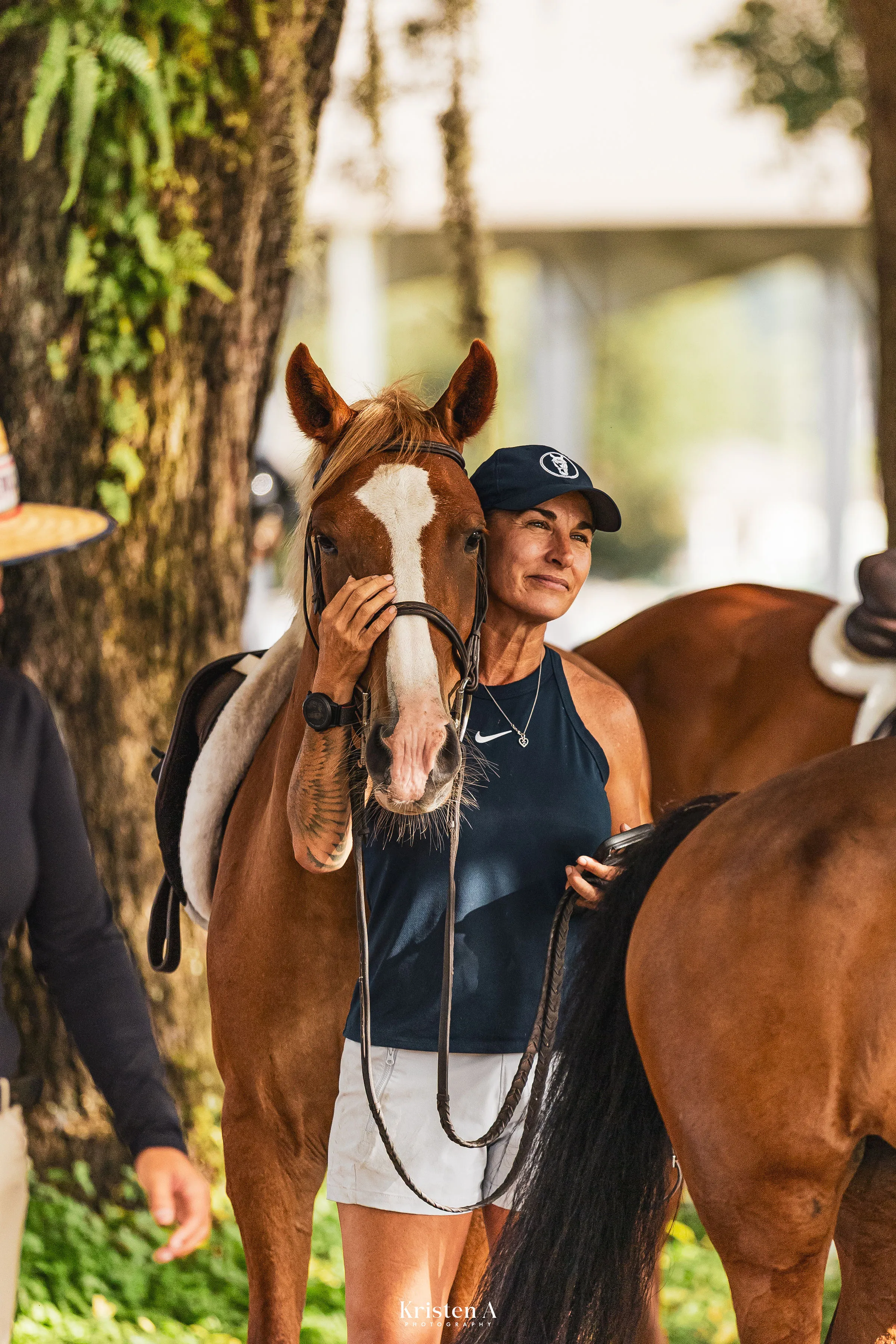 A trainer in a navy cap resting her cheek against a chestnut horse with a white blaze