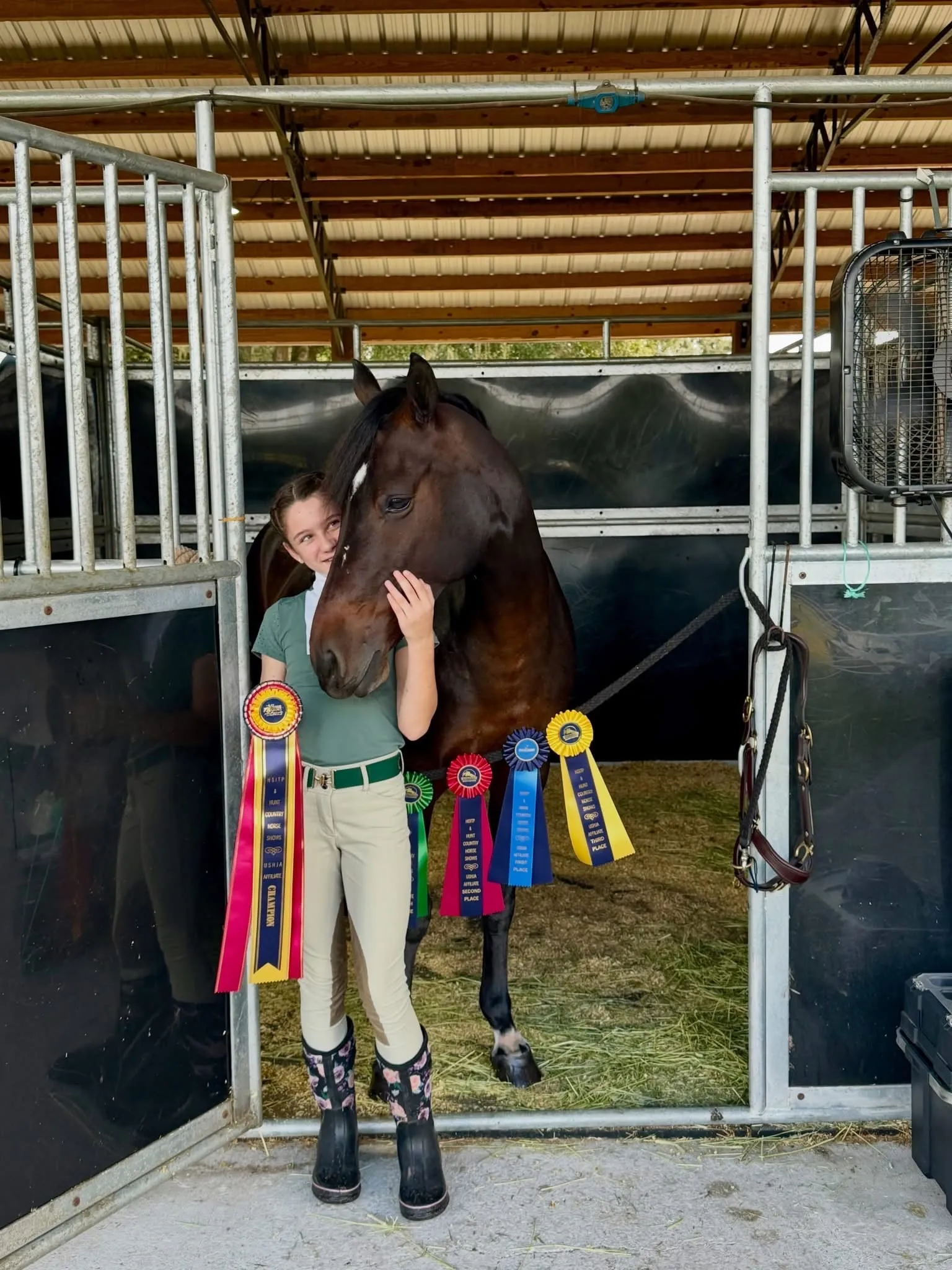 A rider hugging her bay pony at the stall door, ribbons beside them