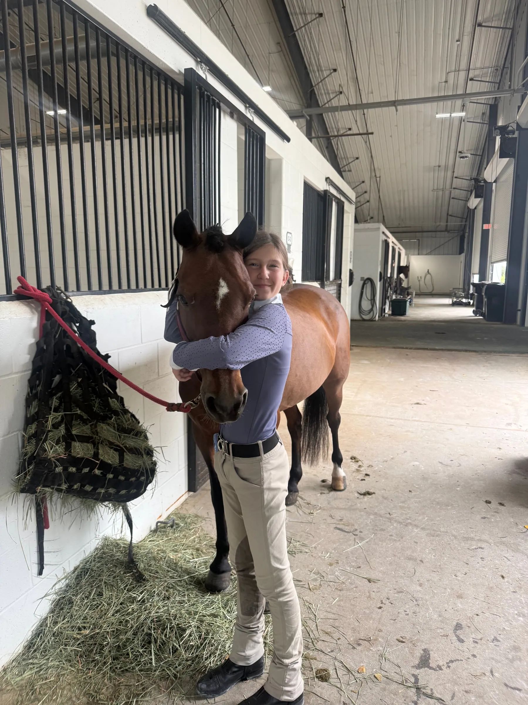 A rider hugging her pony in the barn aisle