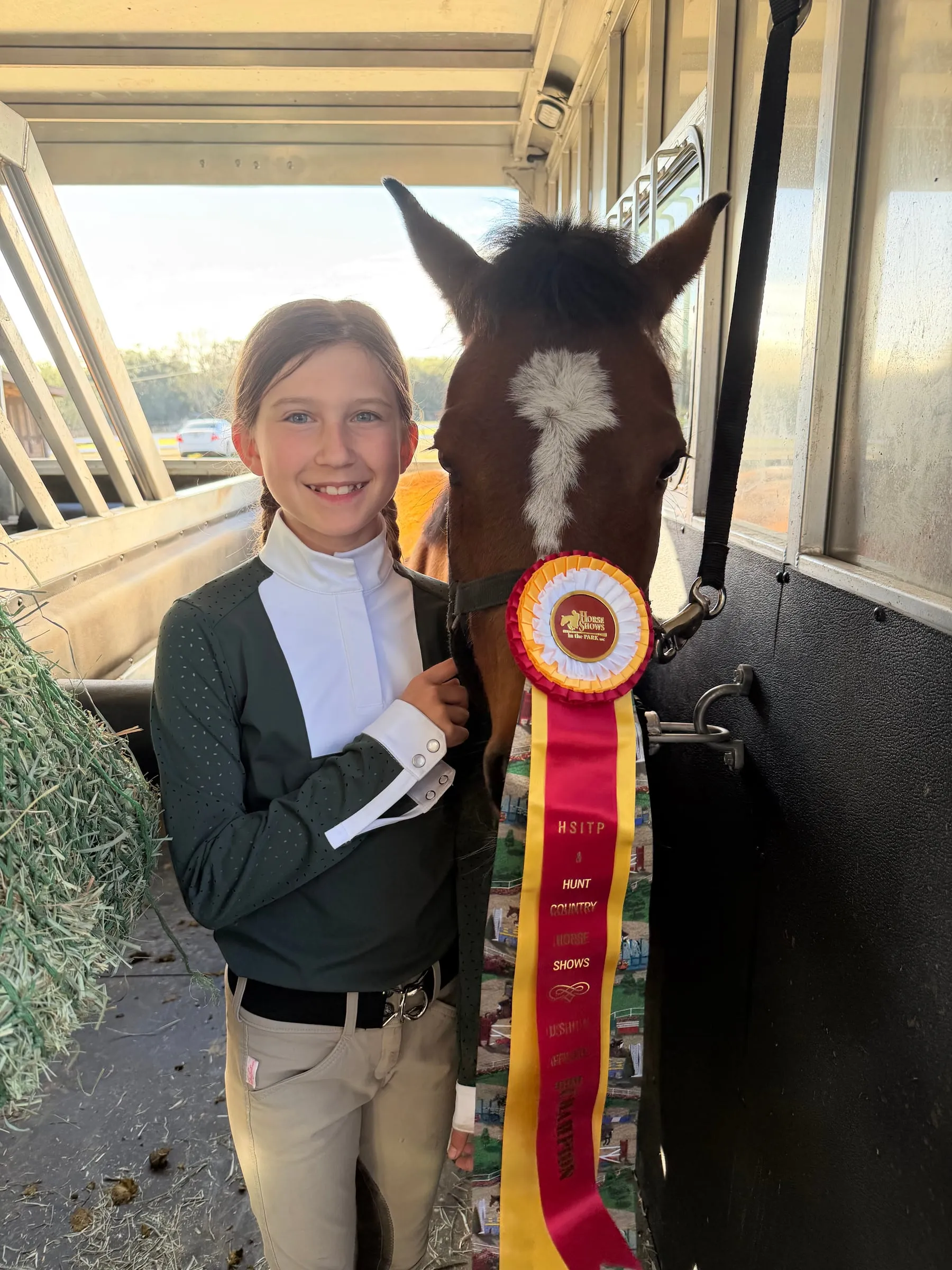 A young rider with her bay pony and a champion ribbon at the stall