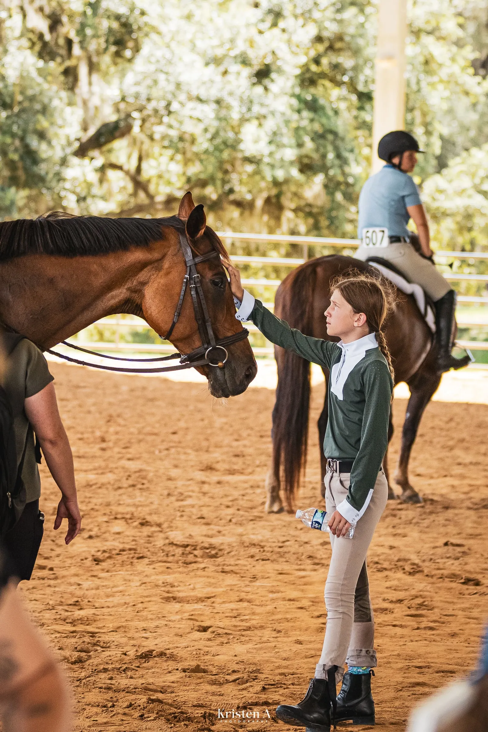 A young rider patting her bay pony in the arena