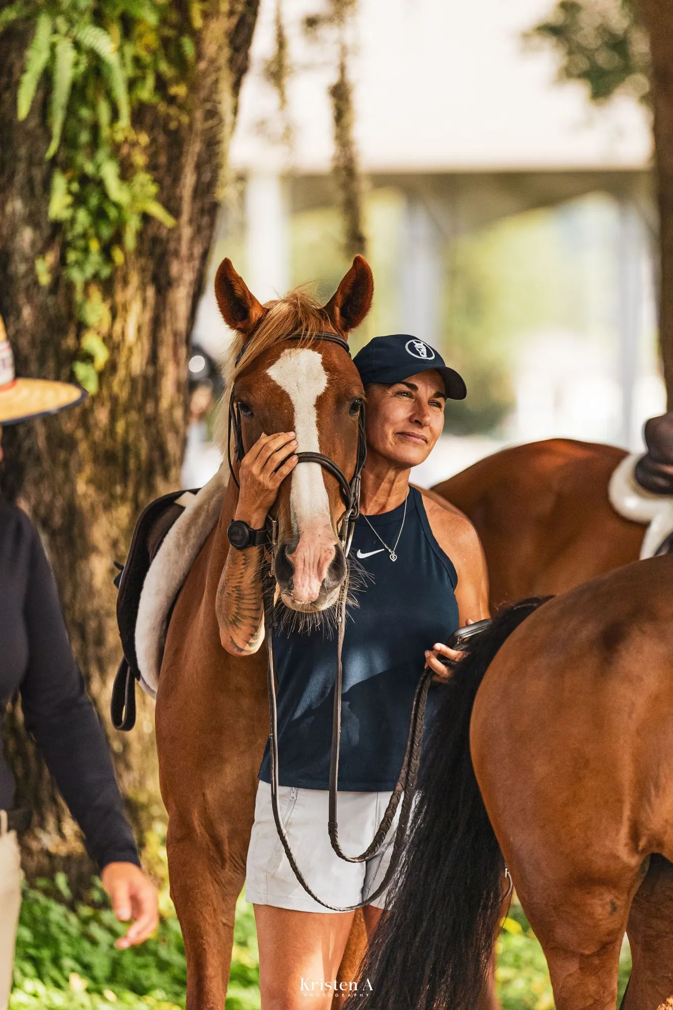 A trainer in a navy cap resting her hand on the blaze of a chestnut pony at a show