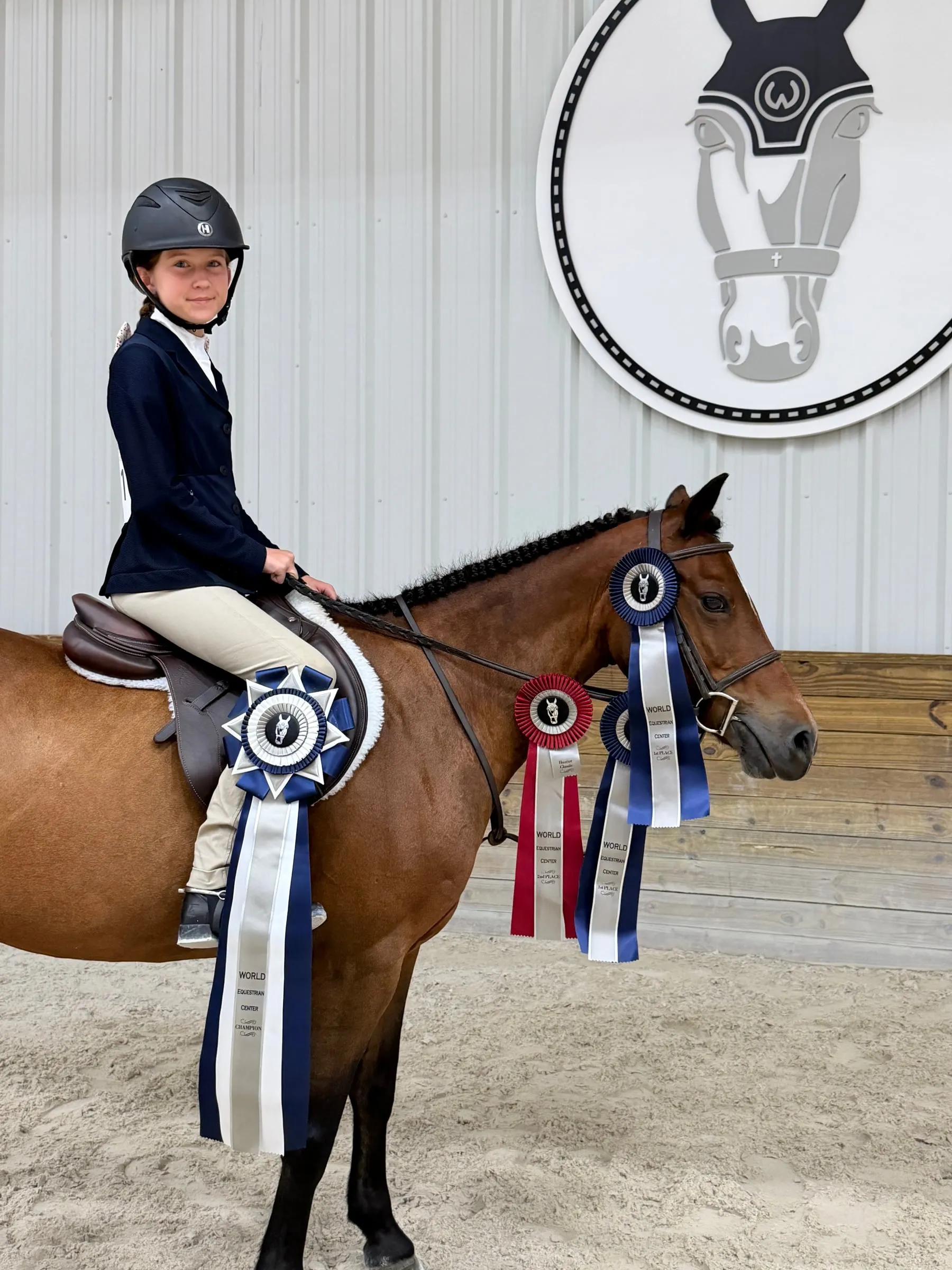 A young rider on a bay pony wearing a champion ribbon and three more ribbons at World Equestrian Center